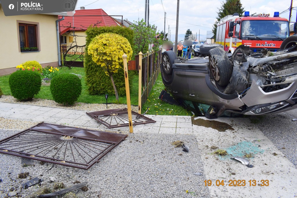 Na snímke je auto, ktoré skončilo po nehode prevrátené na streche. Vidieť je aj rozbitý plot a hasičské auto.