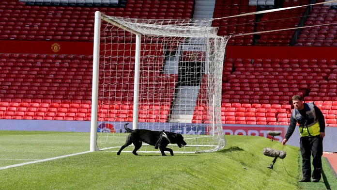 Policajt so psom prehľadáva ihrisko Old Trafford.