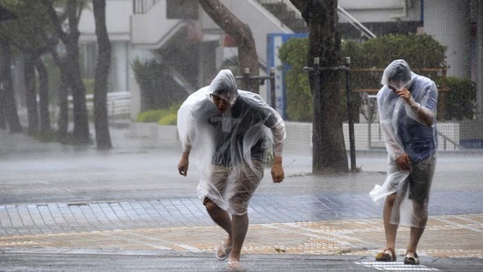 Ľudia kráčajú s ťažkosťami na ulici počas silného vetra a dažďa s príchodom super tajfúnu Vongfong