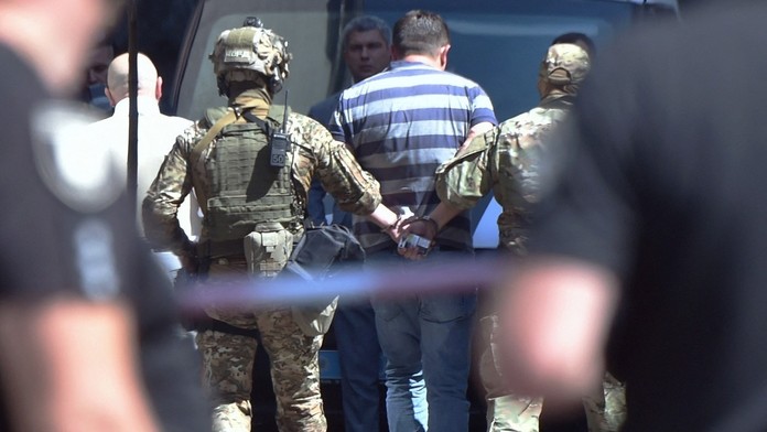 Polícia odvádza muža, ktorý sa vyhrážal, že vo vládnej budove odpáli granát.