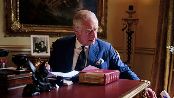 Nový britský kráľ Karol III. sedí za pracovným stolom a vyberá z oficiálnej červenej krabice korešpondenciu.
