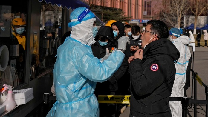 Zdravotník v špeciálnom ochrannom odeve testuje muža na ochorenie COVID-19 v mobilnej testovacej jednotke v Pekingu.