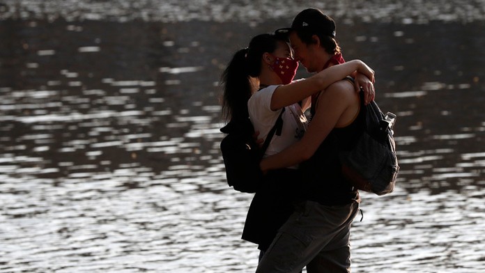 Pár sa objíma počas slnečného počasia pri rieke Vltava v Prahe.