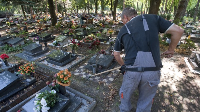 Muž upravuje okolie hrobov.