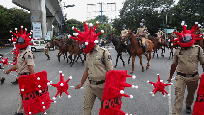 Indickí policajti kráčajú v prilbách v tvare nového typu koronavírusu počas akcie zameranej na prevenciu šírenia koronavírusu.