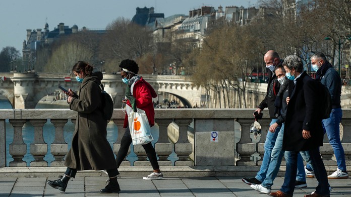 Ľudia s ochrannými rúškami prechádzajú cez most Pont au Change v Paríži.