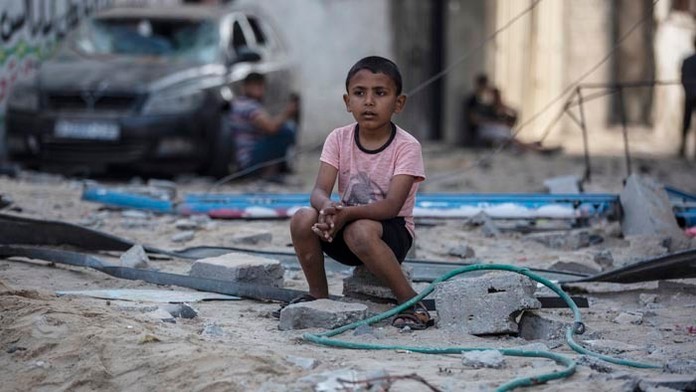 Palestínsky chlapec sedí na troskách zo zničených domov.
