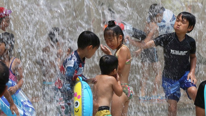 Deti šantia vo fontáne počas horúceho dňa v parku vTokiu. 