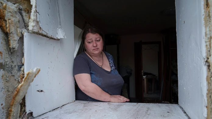 Žena sa pozerá cez okno svojho poškodeného domu po ruskom nálete na obytnú štvrť v Charkove.