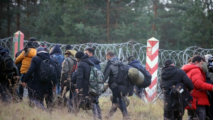 Migranti z Blízkeho východu a iných krajín kráčajú pozdĺž oplotenia s ostnatým drôtom na hranici pri bieloruskej dedine Grodno.
