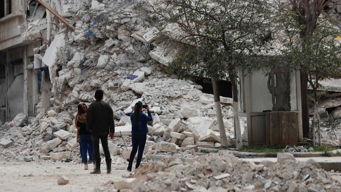 Ľudia stoja pri budove, ktorá sa zrútila v dôsledku nedávneho zemetrasenia v sýrskom meste Aleppo.
