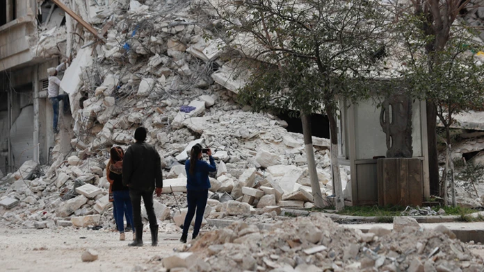 Ľudia stoja pri budove, ktorá sa zrútila v dôsledku nedávneho zemetrasenia v sýrskom meste Aleppo.
