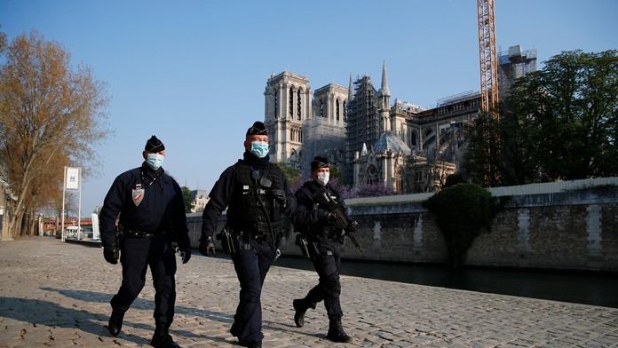 Policajti hliadkujú pozdĺž rieky Seiny, v pozadí katedrála Notre-Dame počas druhého výročia ničivého požiaru.