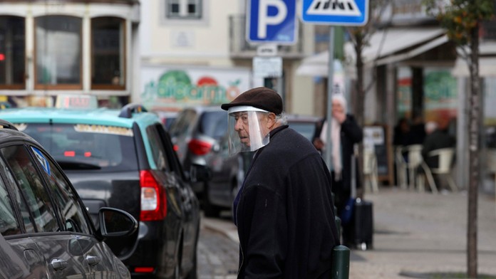 Starší muž s ochranným štítom na hlave kráča ulicami Lisabonu.