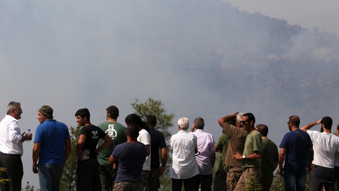 Ľudia sledujú vrtuľník počas hasenia lesného požiaru v oblasti juhozápadne od Nikózie.