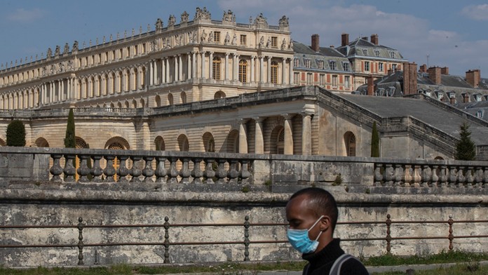 Muž s ochranným rúškom kráča vedľa zámku Versailles.