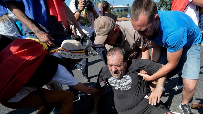 Demonštranti pomáhajú vstať mužovi, ktorý spadol, keď sa pokúšal prejsť cez zástup policajtov na protivládnom proteste v Bukureš