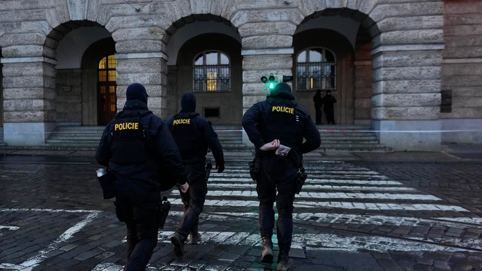 Policajti kráčajú pred budovou Filozofickej fakulty Univerzity Karlovej (FF UK) po streľbe v centre Prahy 22. decembra 2023. 