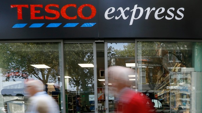 Ľudia prechádzajú okolo obchodu Tesco express.