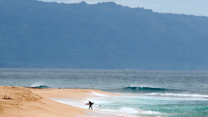 Surfer vychádza z oceánu na severnom pobreží Oahu neďaleko Haleiwa na Havaji.