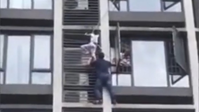 Otec zachraňuje syna visiaceho z klimatizácie na priečelí budovy.