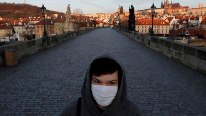 Mladý muž s ochranným rúškom kráča po Karlovom moste v Prahe.