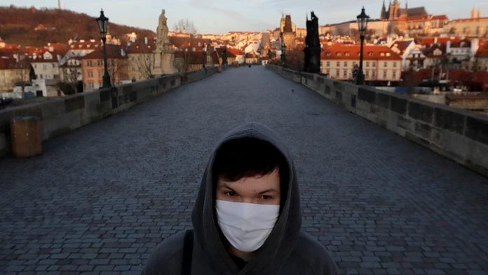 Mladý muž s ochranným rúškom kráča po Karlovom moste v Prahe.