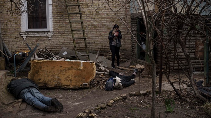 Žena kráča medzi telami svojho manžela, brata a ďalšieho muža, ktorých zabili pred jej domom v Buči.