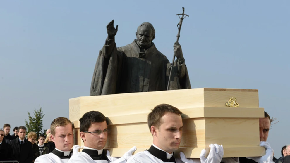 Seminaristi nesú truhlu s pozostatkami kardinála Jána Chryzosta Korca okolo sochy  Jána Pavla II.