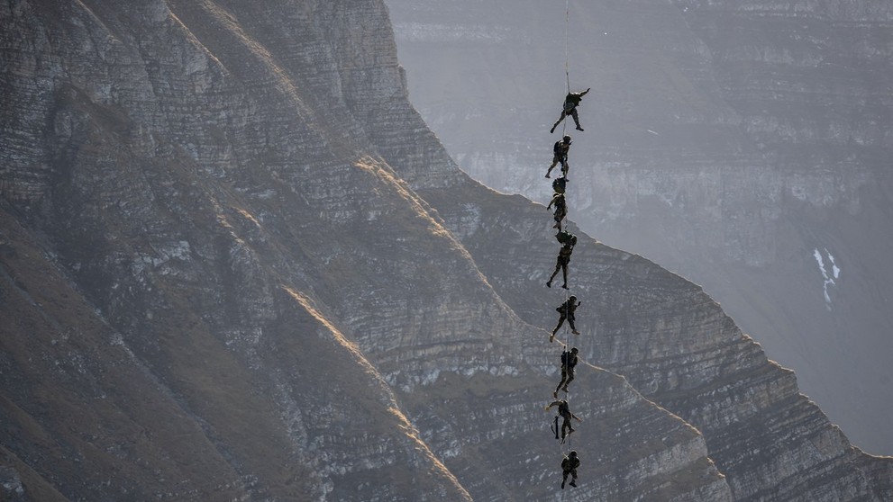 Príslušníci špeciálnych jednotiek švajčiarskej armády visia na lane počas leteckej šou nad lyžiarskym strediskom Axalp.