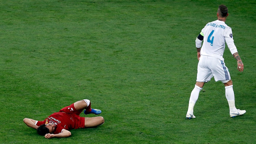 Salah leží v bolestiach na trávniku po zrážke s Ramosom.