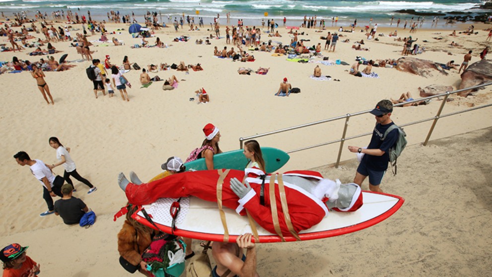 Figurína Santa Clausa je pripevnená na surfe, aby ju ľahšie prepravili po pláži Bondi Beach v Austrálii.