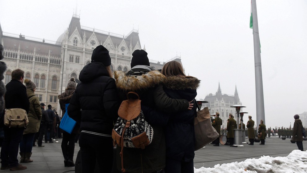 Ľudia sledujú spúšťanie štátnej vlajky na pol žrde.