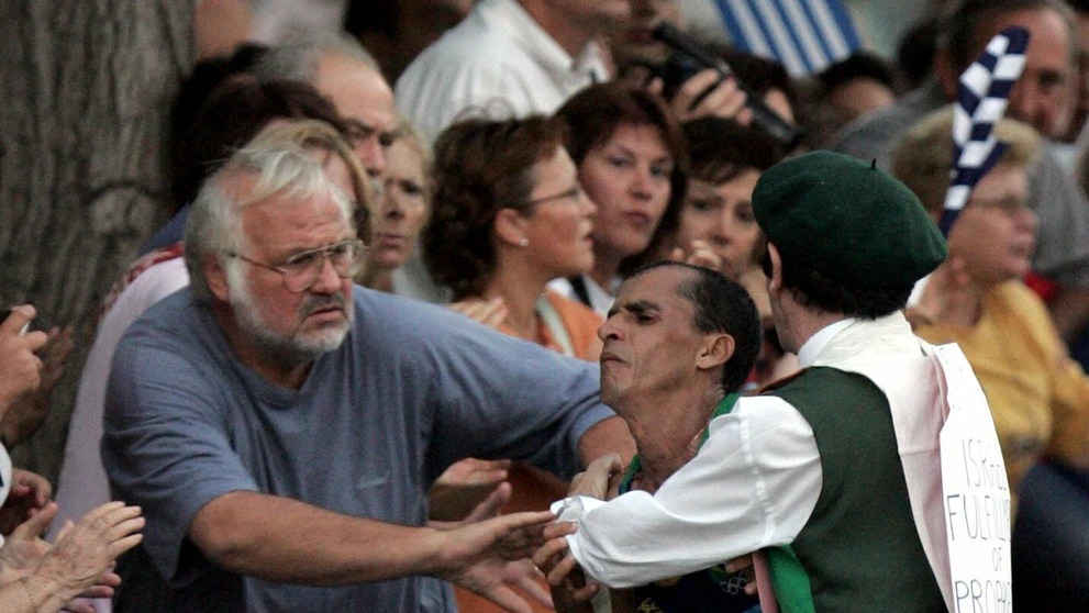 Neznámy muž v kostýme napadá favorita pretekov, brazílskeho atléta Vanderleia De Limu, na maratónskej trati v Aténach.