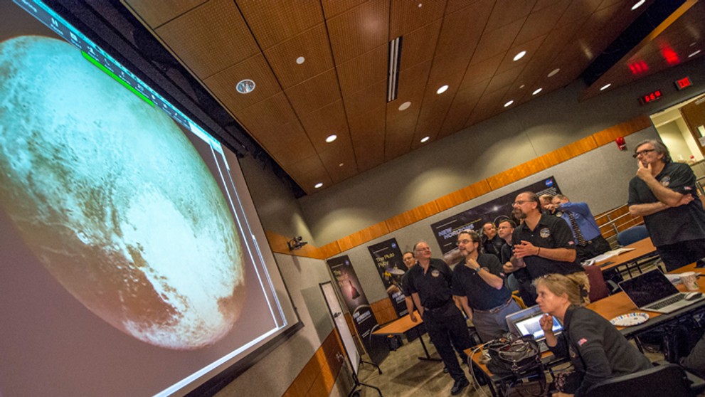 Členovia vedeckého tímu New Horizons pozerajú na Pluto.
