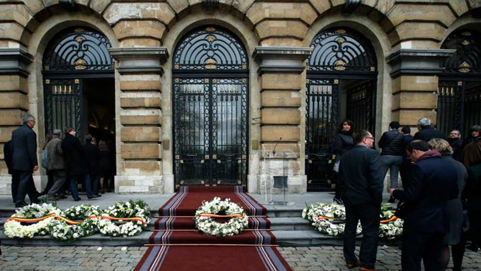 Belgickí poslanci kráčajú okolo vencov položených na pamiatku obetí teroristických útokov pred budovou parlamentu v Bruseli.