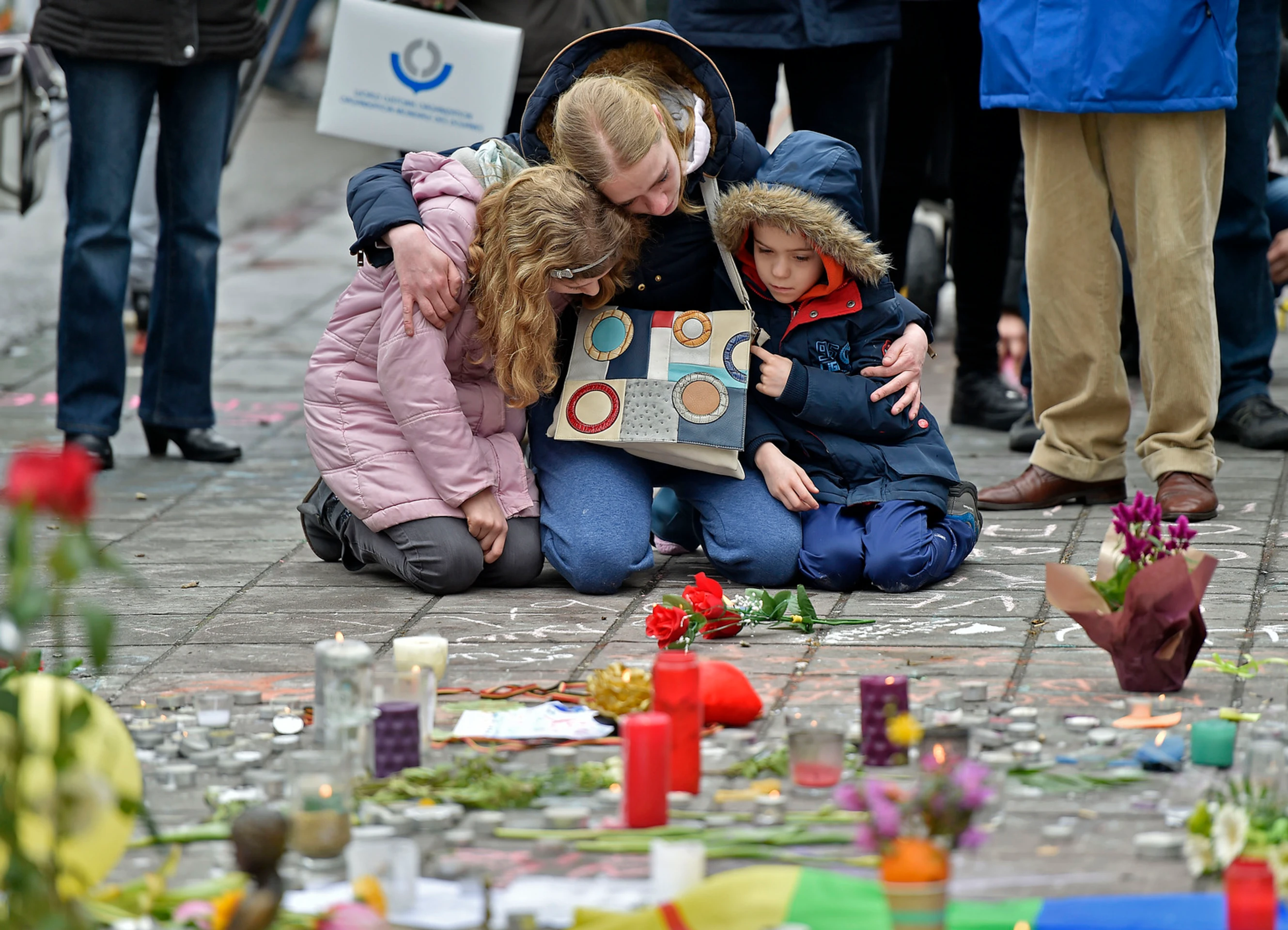 Žena s deťmí kľačí na pamiatku obetí  bombových útokov v Bruseli.