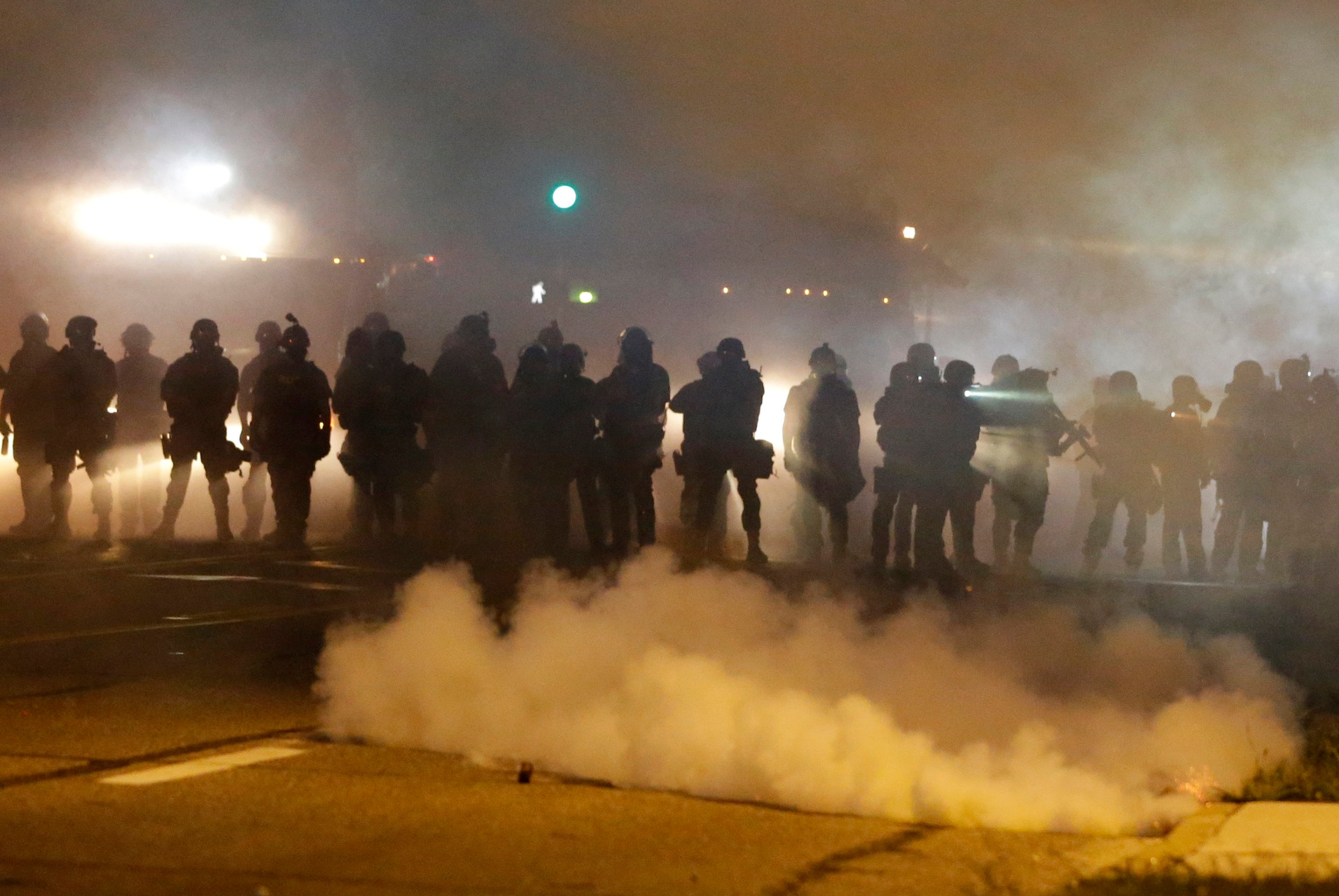 Príslušníci polície kráčajú v hustom dyme pošas rasovo motivovanej demonštrácie v americkom meste Ferguson.