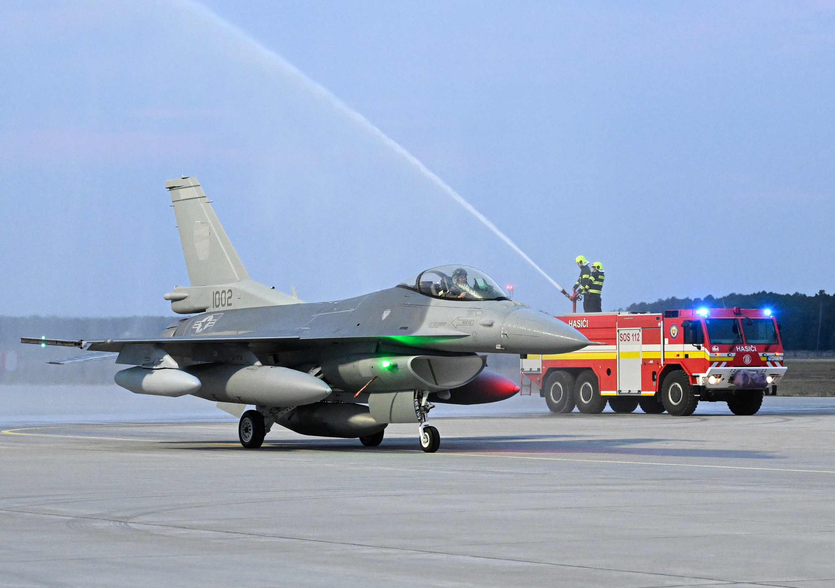 Jedna z dvoch stíhačiek F-16 symbolicky prechádza tzv. slávobránou z hasičských striekačiek v priestoroch Leteckej základne Malacky-Kuchyňa.