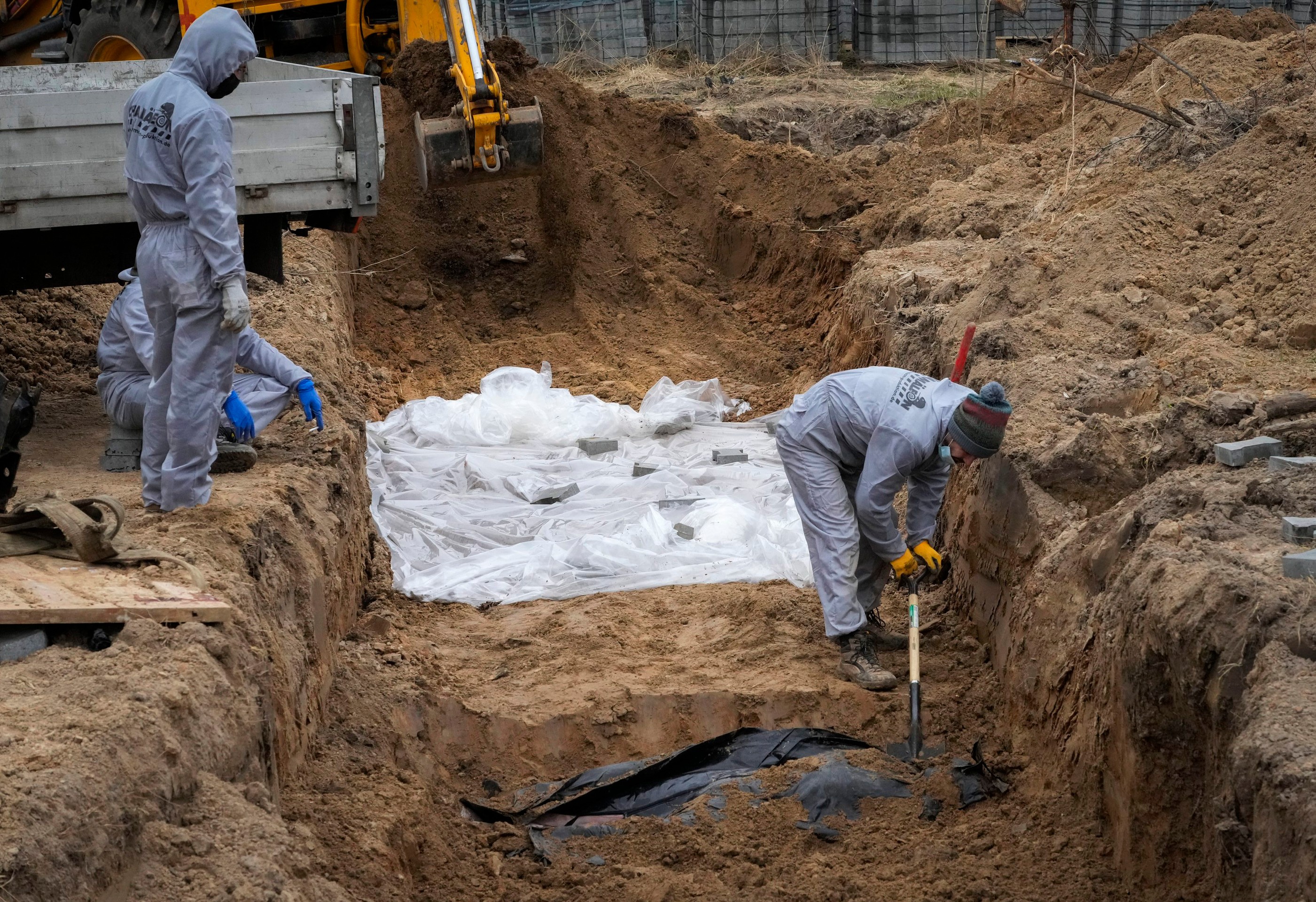Muži v ochranných odevoch exhumujú telá civilistov v ukrajinskom meste Buča.