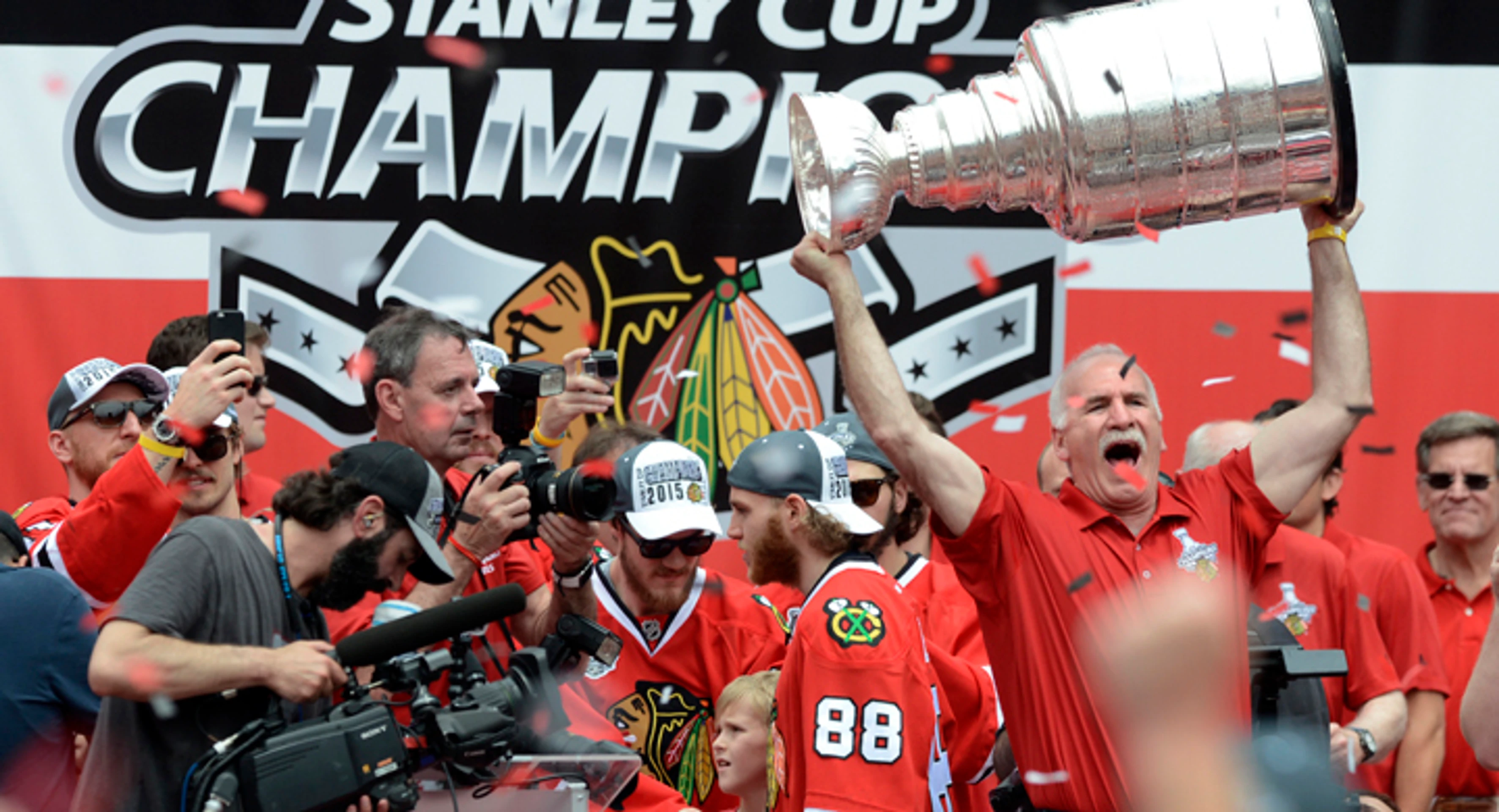 Tréner Chicaga Blackhawks Joel Quenneville dvíha nad hlavu Stanleyho pohár počas osláv titulu, Hossa si všetko fotí.