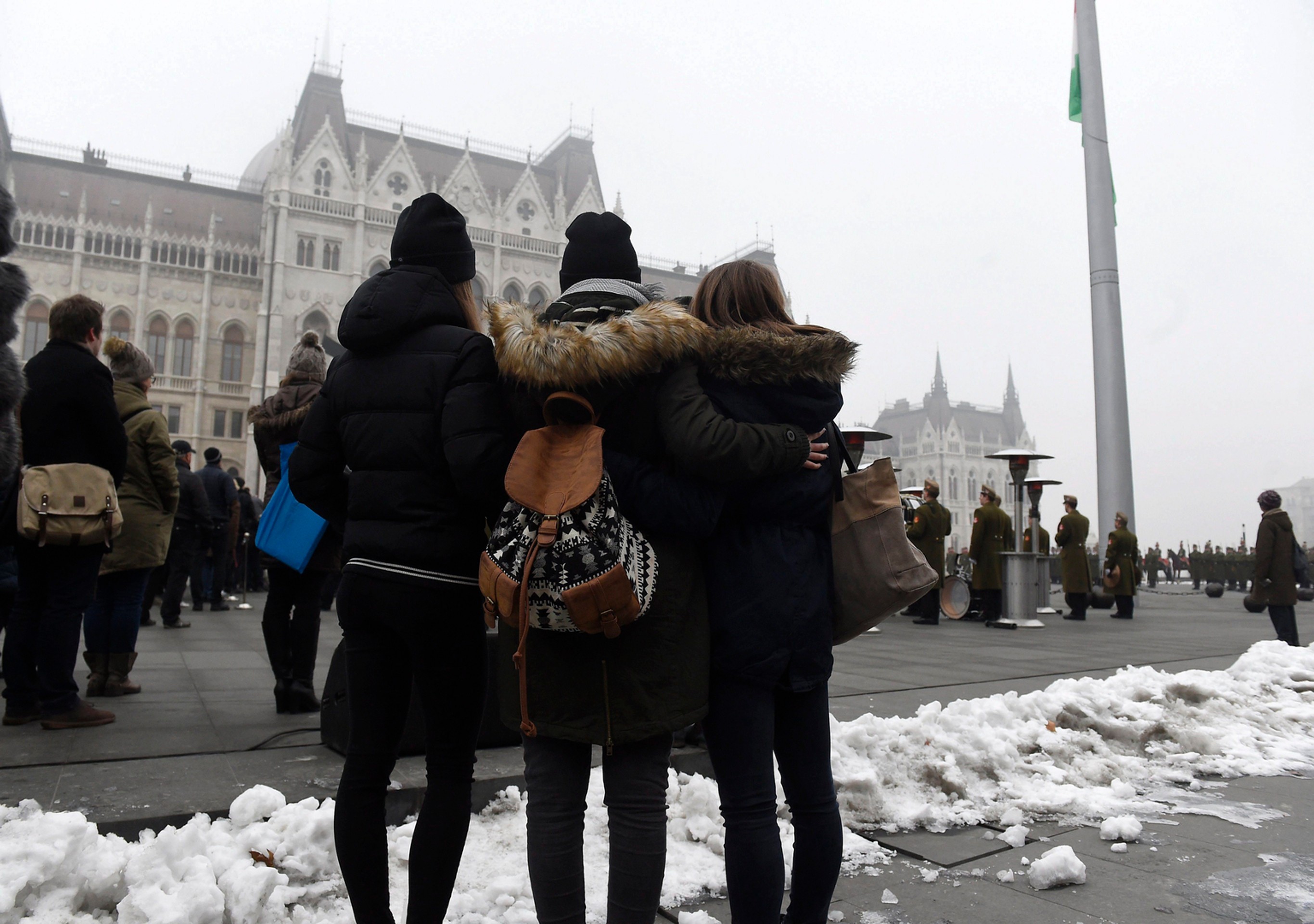 Ľudia sledujú spúšťanie štátnej vlajky na pol žrde.