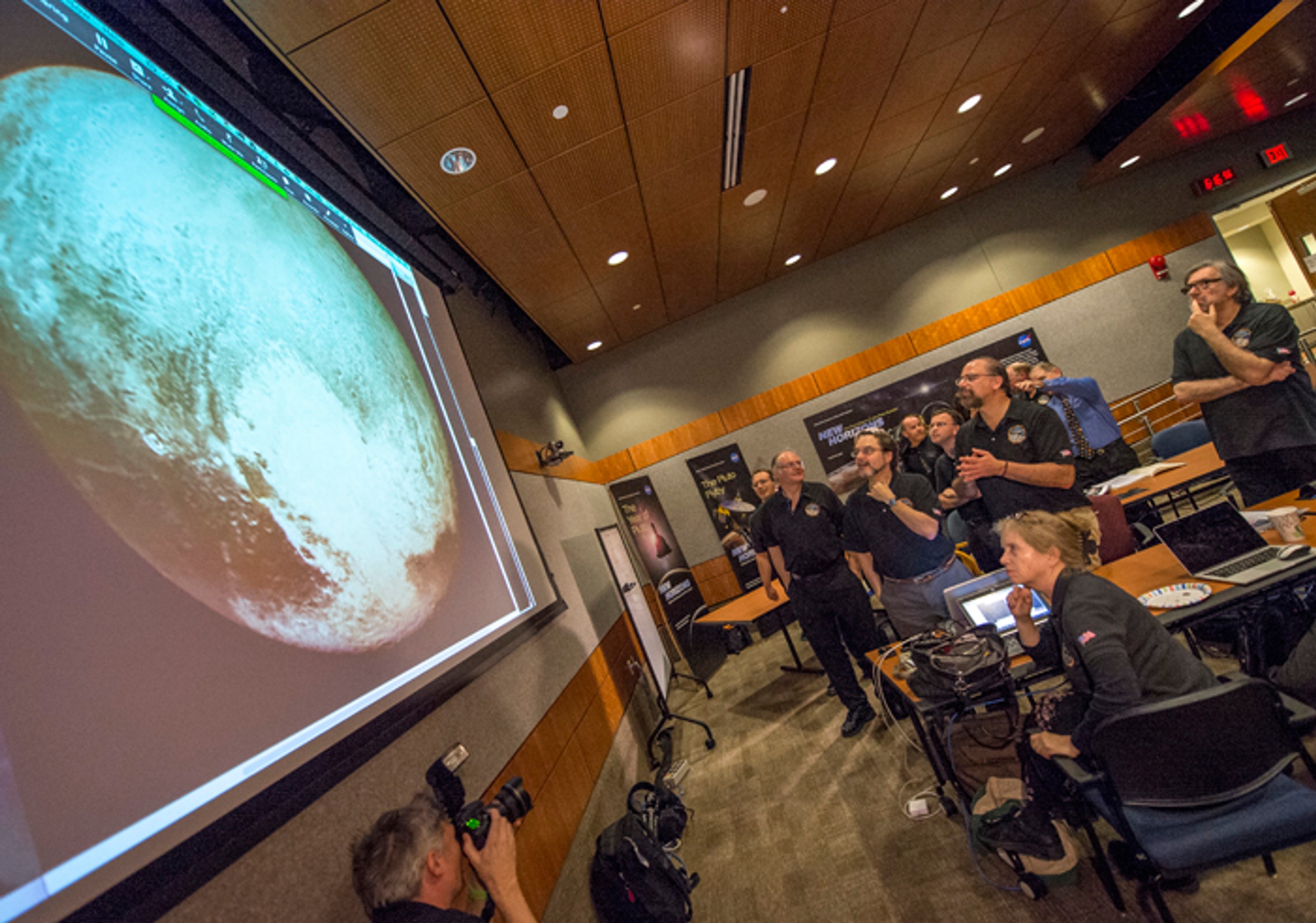 Členovia vedeckého tímu New Horizons pozerajú na Pluto.