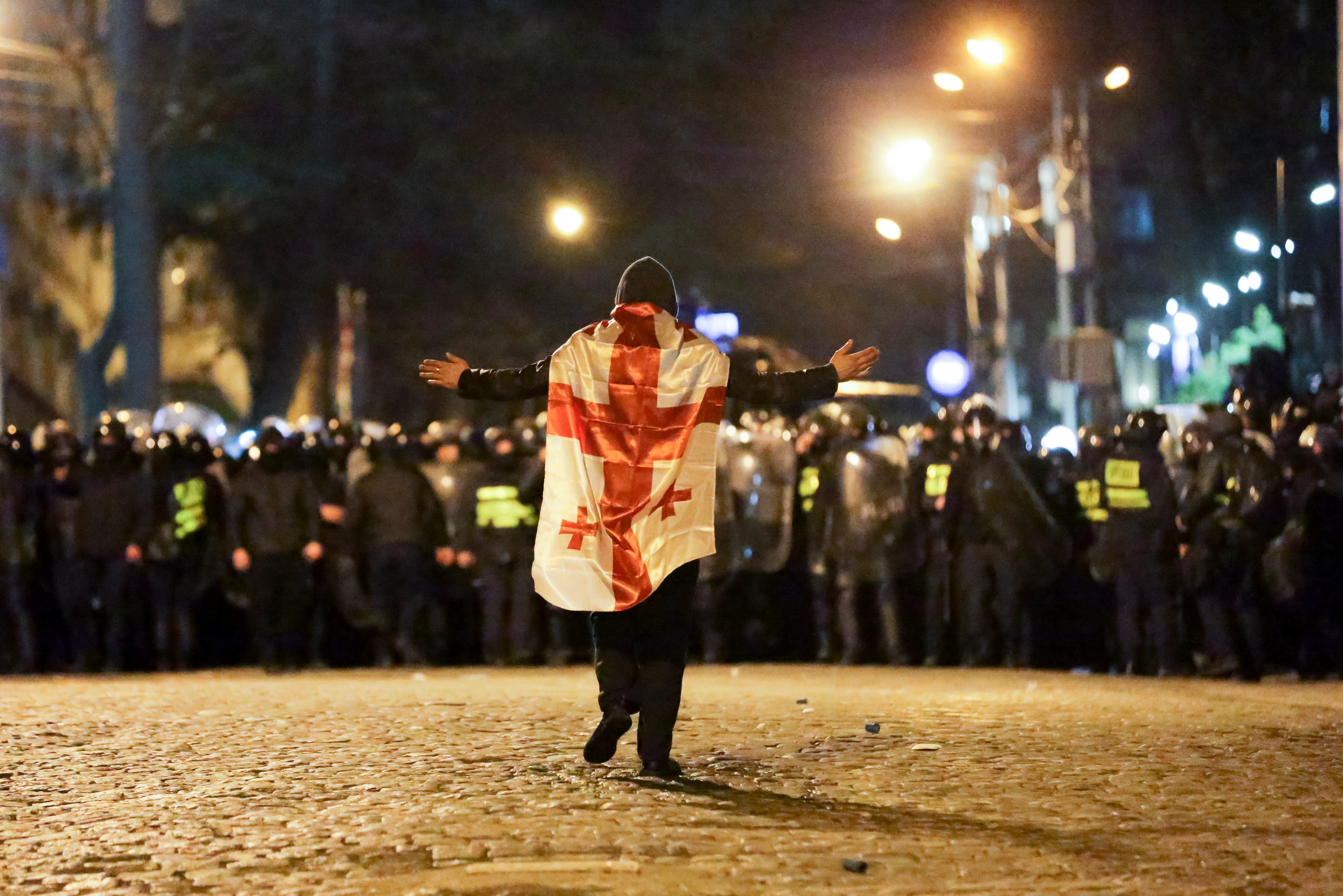 Demonštrant s gruzínskou vlajkou kráča k policajtom počas protestu pred budovou parlamentu v Tbilisi.